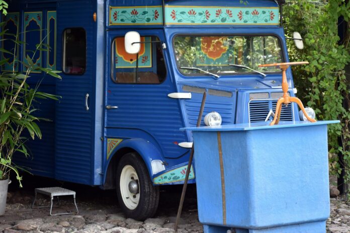 A small blue bus parked next to a bush